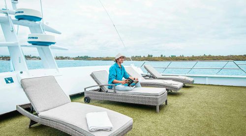 tourist reading a book in the deck of anahi catamaran yacht of galapagos islands
