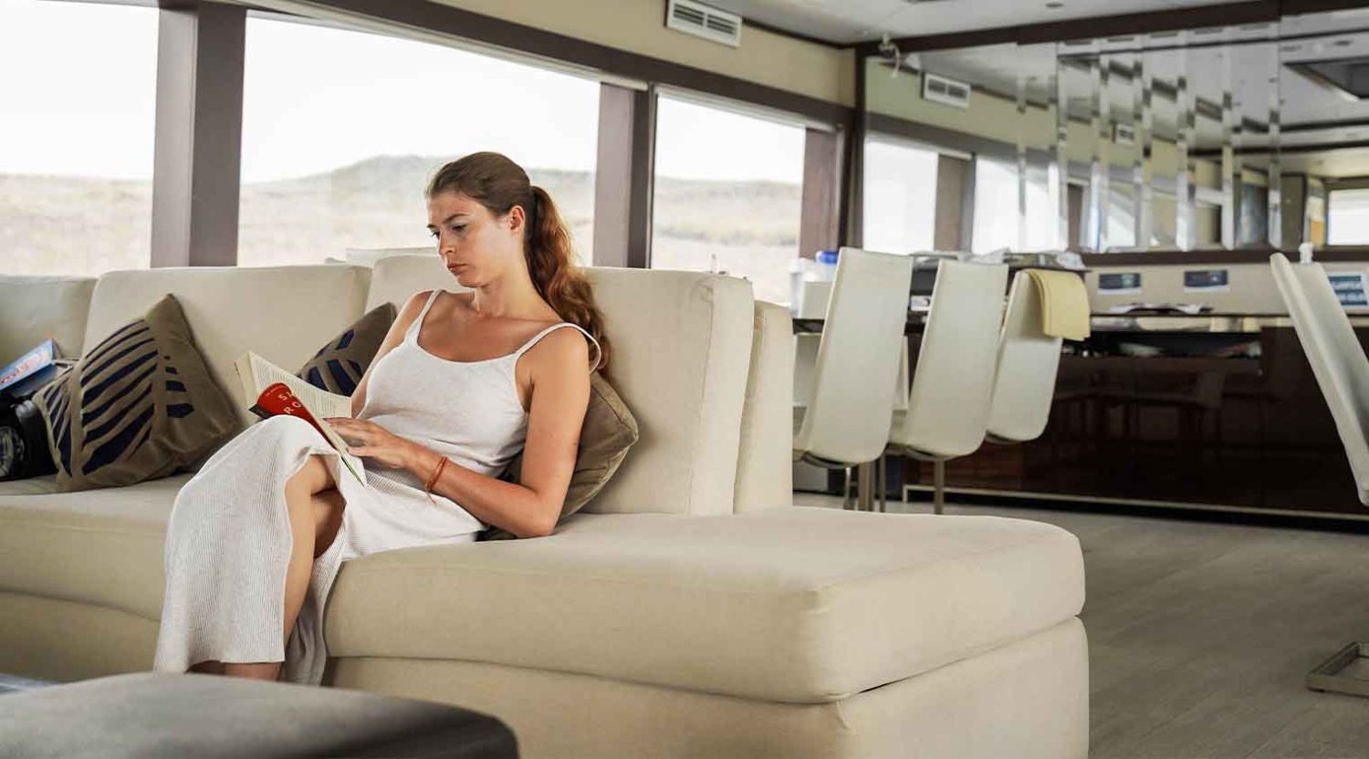 woman reading in Grand Majestic Galapagos Yacht living room of galapagos islands tours